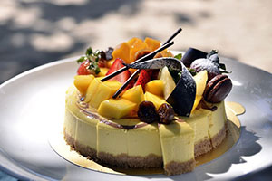 A cheesecake adorned with various fruits such as mango and strawberries, as well as chocolate, figs and macarons dusted with icing sugar