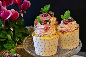 Three cupcakes on a glass platter with pink icing and adorned with berries