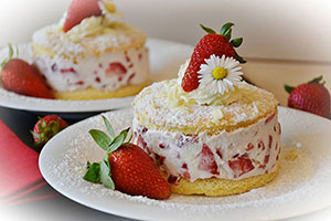 Small strawberry cakes on plates adorned with fresh cream, strawberries and a daisy all lightly dusted in icing sugar