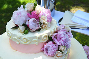 A pink and white decorated cake adorned with roses and peonies